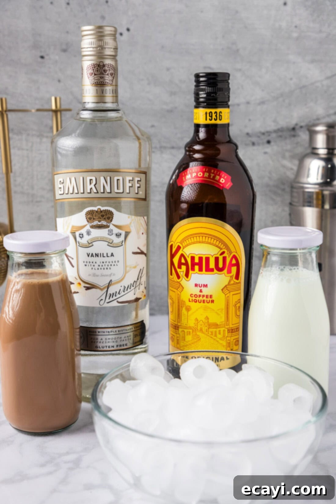 Cold Buzz Coffee 4 Ingredients for Spiked Iced Coffee laid out on a table, including bottles of Kahlua and vanilla vodka, a carton of iced coffee, and a pitcher of half and half.