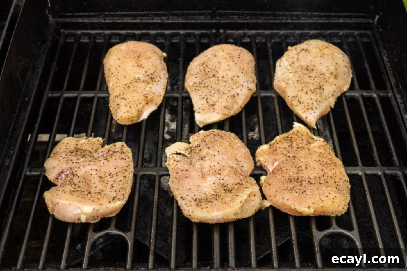 Crispy Chicken Sandwich 6 Seasoned chicken breasts cooking on a hot grill, showing the initial stages of searing and developing grill marks.