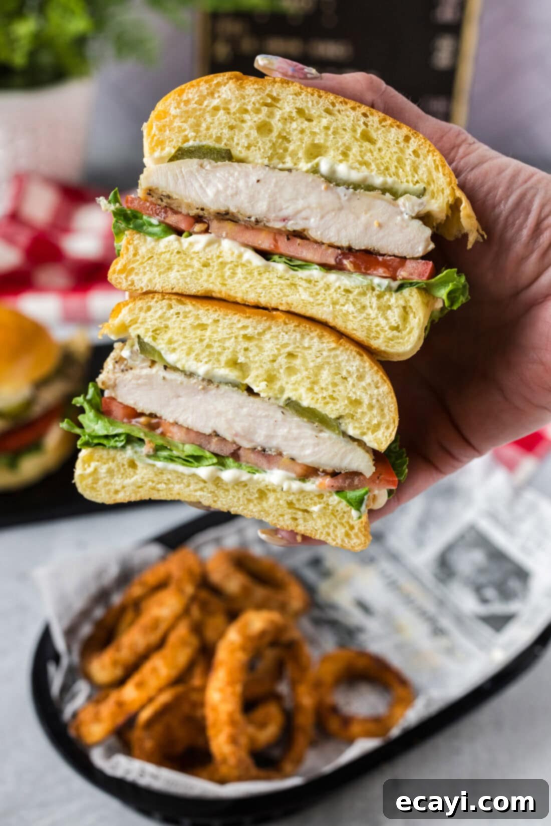 Crispy Chicken Sandwich 8 A hand holding a grilled chicken sandwich cut in half, revealing its juicy interior and layers of fresh toppings.