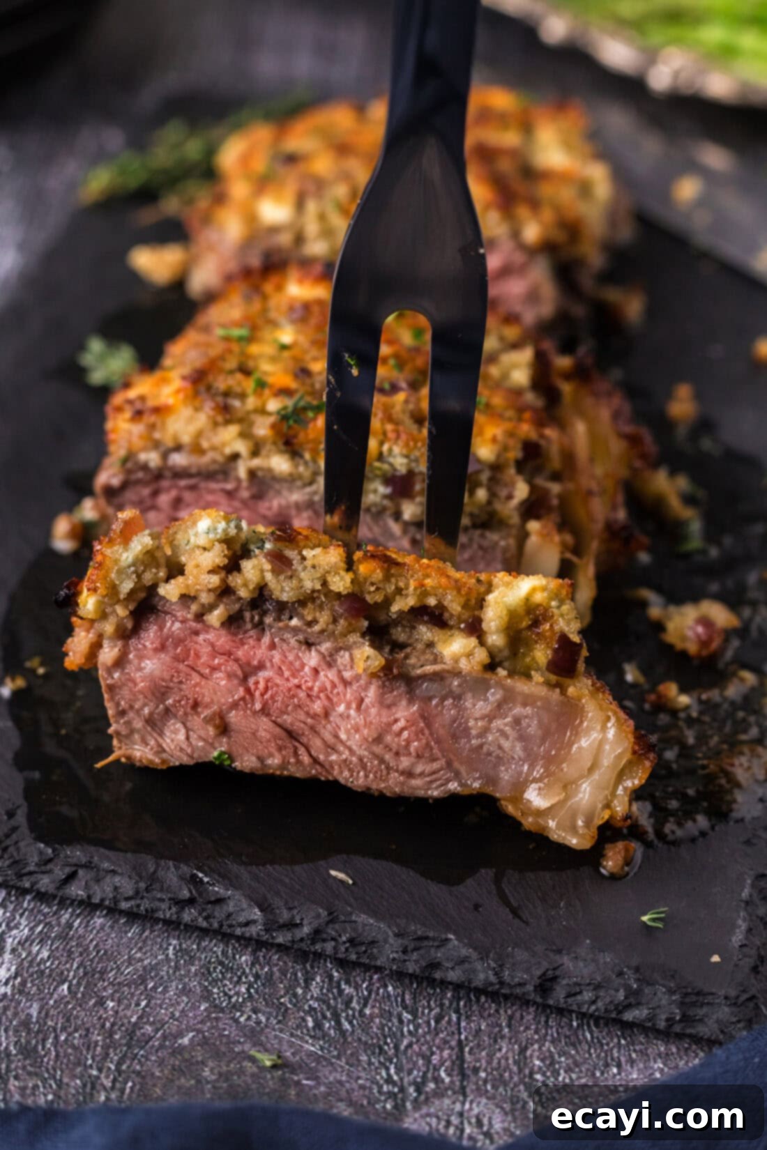 Signature Blue Cheese Crusted Steak 2 A meat fork lifts a tender piece of perfectly cooked Blue Cheese Crusted Steak, showcasing its golden, cheesy crust and juicy interior.