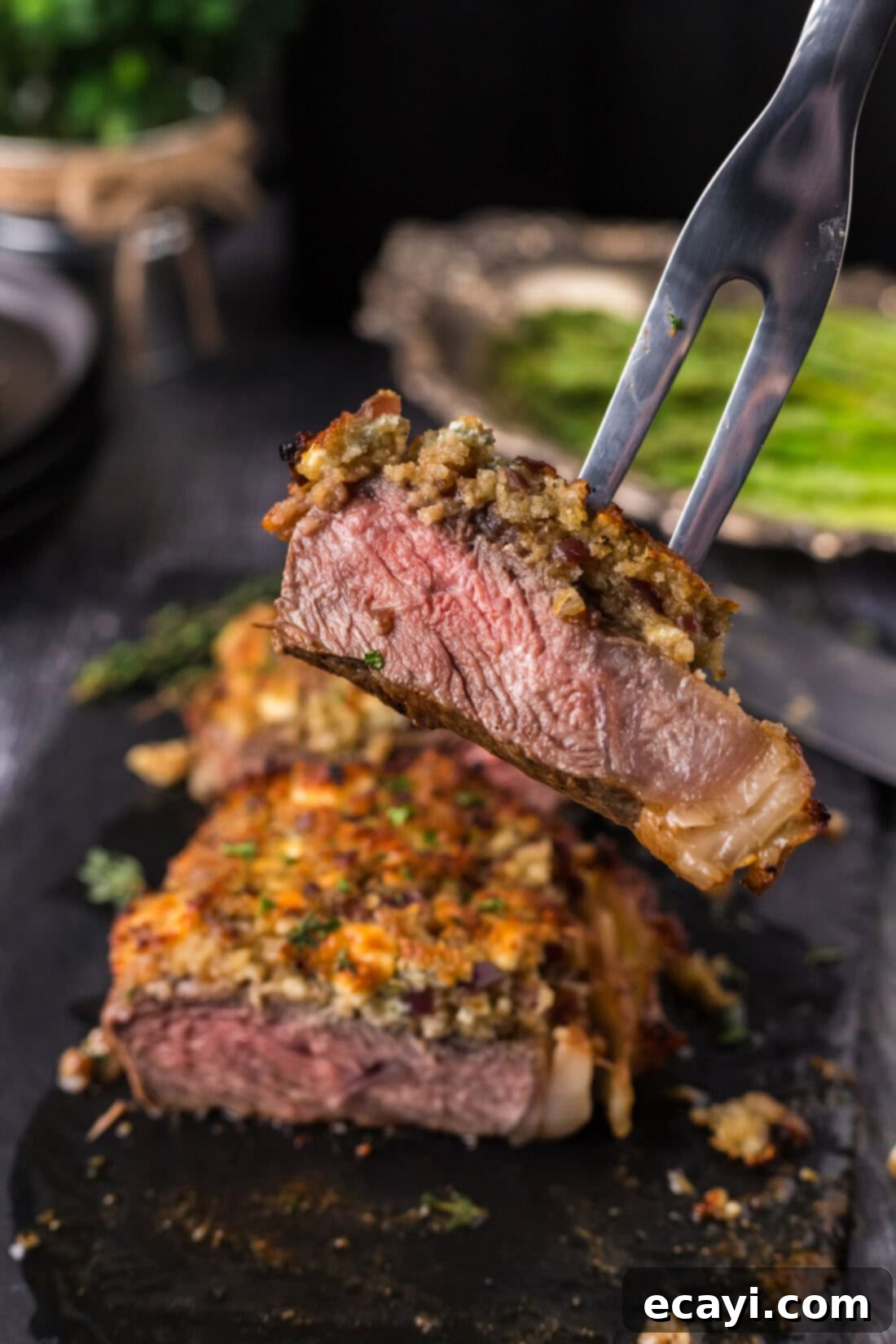 Signature Blue Cheese Crusted Steak 12 A meat fork lifting a beautifully crusted piece of Blue Cheese Crusted Steak, revealing its tender, juicy interior.