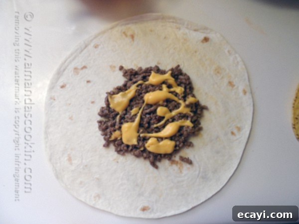 The Ultimate At-Home Crunchwrap 4 Warm nacho cheese sauce being drizzled over a layer of seasoned ground beef spread on a large flour tortilla.
