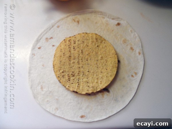 The Ultimate At-Home Crunchwrap 5 A crispy tostada shell being placed on top of the nacho cheese and ground beef layer on a flour tortilla.