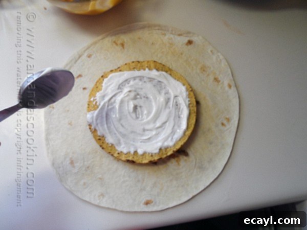 The Ultimate At-Home Crunchwrap 6 Sour cream being spread evenly over the top of the tostada shell.