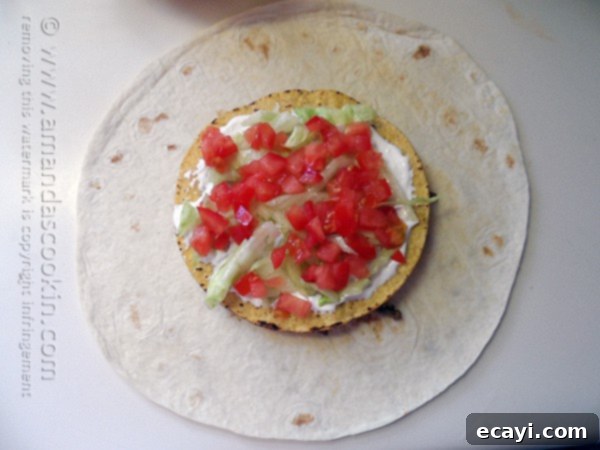 The Ultimate At-Home Crunchwrap 7 Shredded lettuce and diced tomatoes sprinkled over the sour cream layer on the tostada shell.