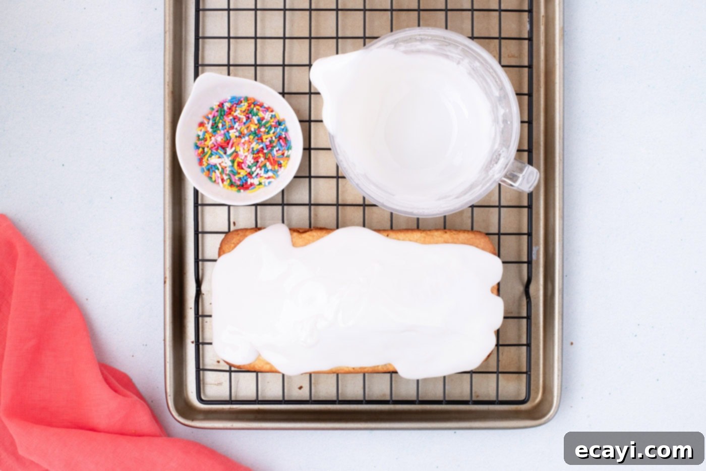 2-Ingredient Ice Cream Bread 10 A freshly baked quick bread, covered in a beautiful white vanilla glaze, with a bowl of colorful sprinkles nearby.