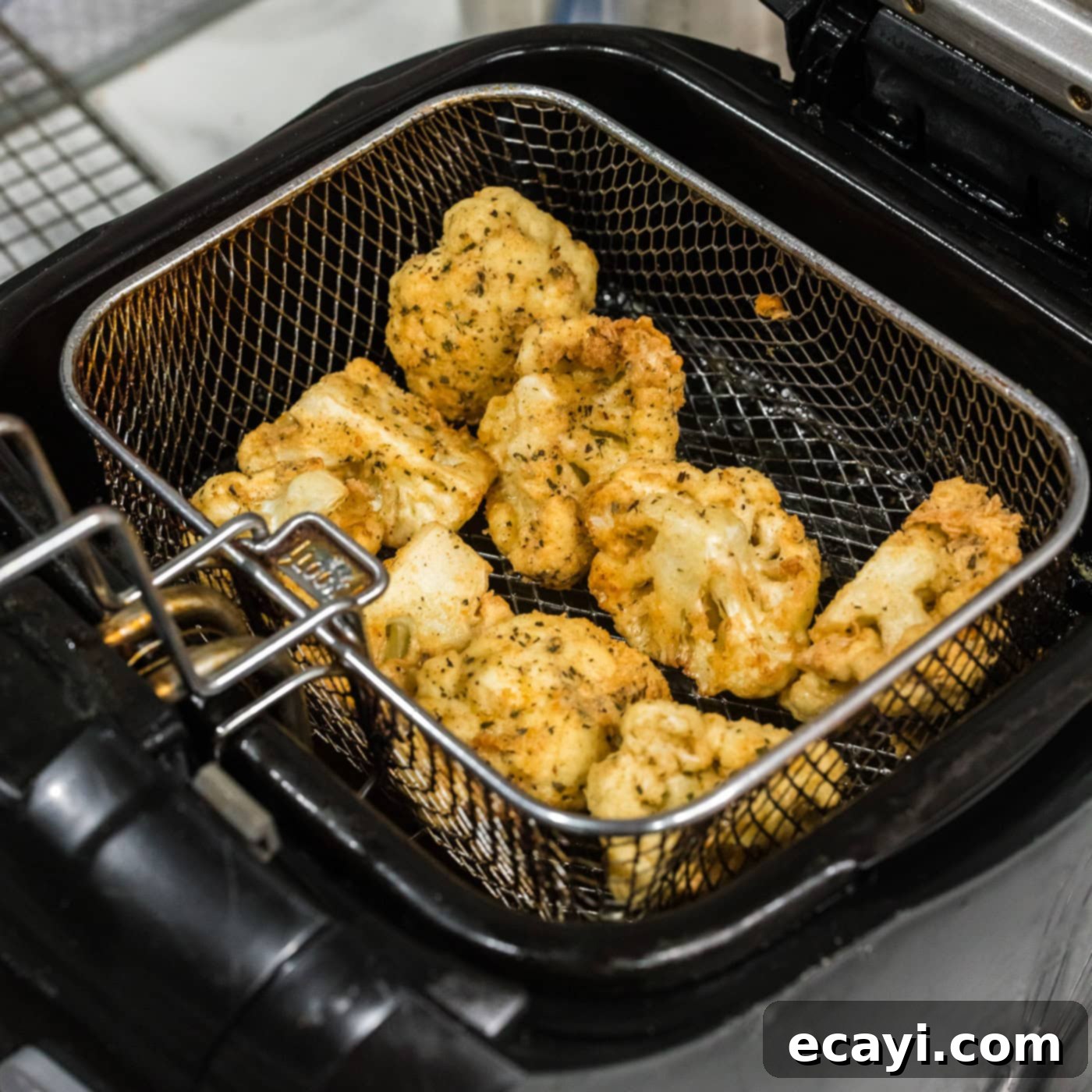 Golden Fried Florets 11 Deep fried cauliflower florets, golden and crispy, being lifted from the hot oil in a fryer basket