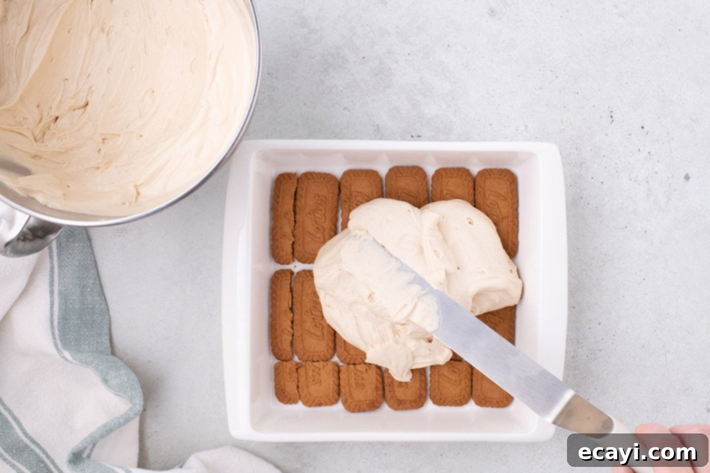 No-Bake Biscoff Bliss 10 spreading Biscoff cream cheese mixture over cookies in a baking dish