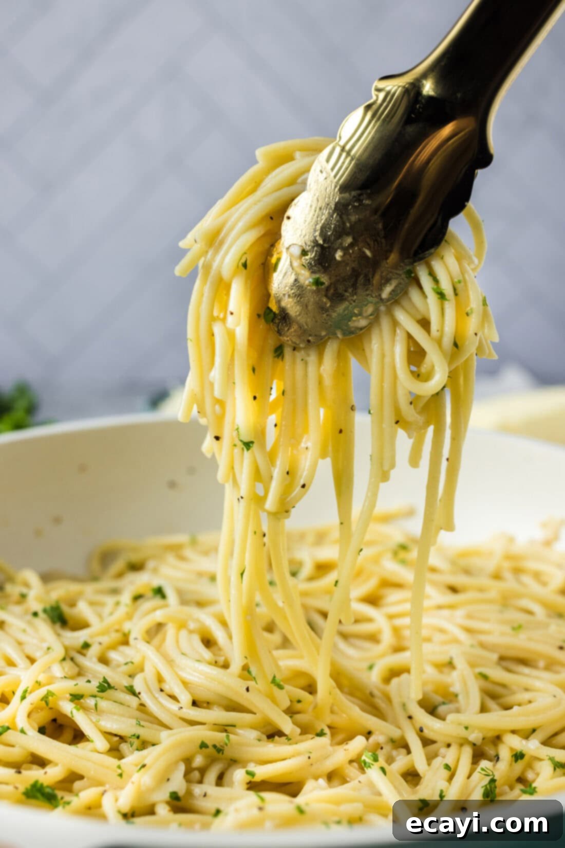 Irresistible Garlic Butter Pasta 3 Tongs lifting strands of perfectly coated garlic butter pasta from a large skillet, showcasing the rich, golden sauce.