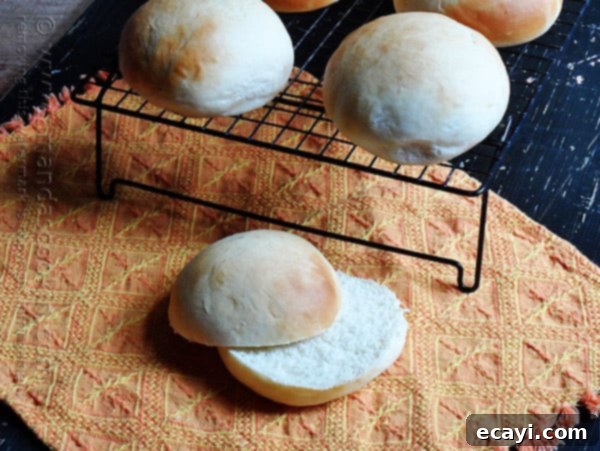 Soft and Fluffy Homemade Burger Buns 4 A trio of homemade hamburger buns, brushed with melted butter and glistening, on a cooling rack.