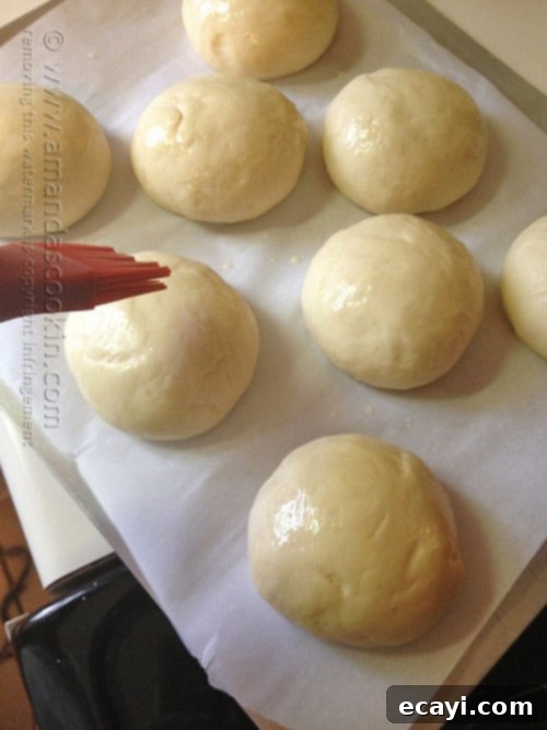 Soft and Fluffy Homemade Burger Buns 8 Melted butter being brushed generously over the tops of unbaked hamburger buns.