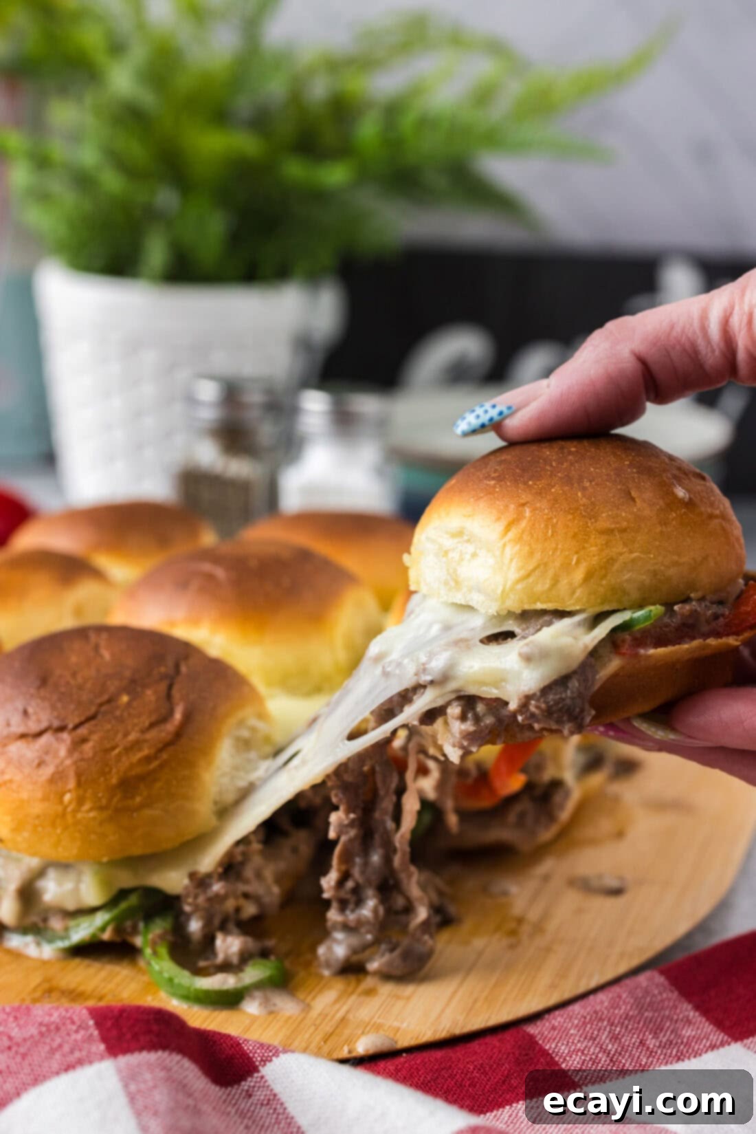 Cheesesteak Slider Bites 2 Hand pulling up a cheesy Philly Cheesesteak Slider from the board of Philly Cheesesteak Sliders