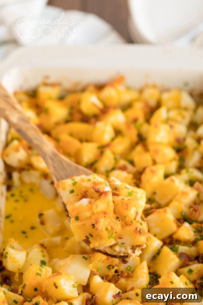 Cheddar, Monterey jack and smoked mozzarella come together in this delicious three cheese potatoes dish. Perfect to serve a crowd or to bring to a potluck. A wooden spoon scoops a generous portion of cheesy bacon potatoes from a rustic casserole dish, revealing the creamy texture and melted cheese inside.