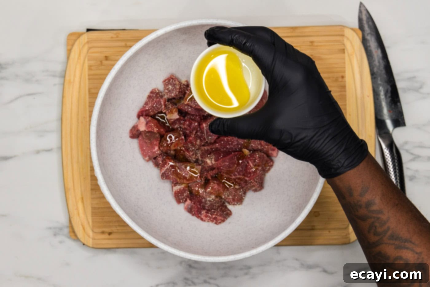 Easy Instant Pot Beef Tips and Gravy 5 hand holding bowl of olive oil over cubes of meat