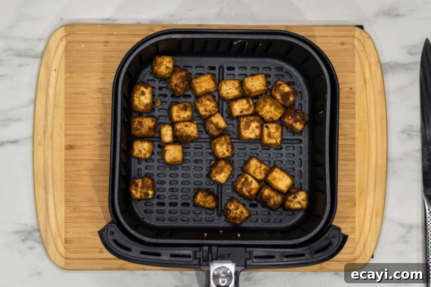 Crispy Air Fryer Tofu 10 air fried tofu cubes in an air fryer basket, now golden and crispy