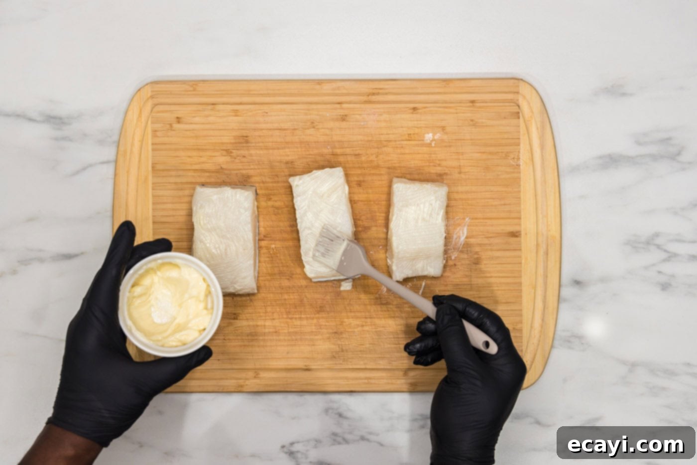 Perfectly Baked Chilean Sea Bass 5 Brushing Chilean sea bass with softened butter on a cutting board, preparing it for seasoning and baking.