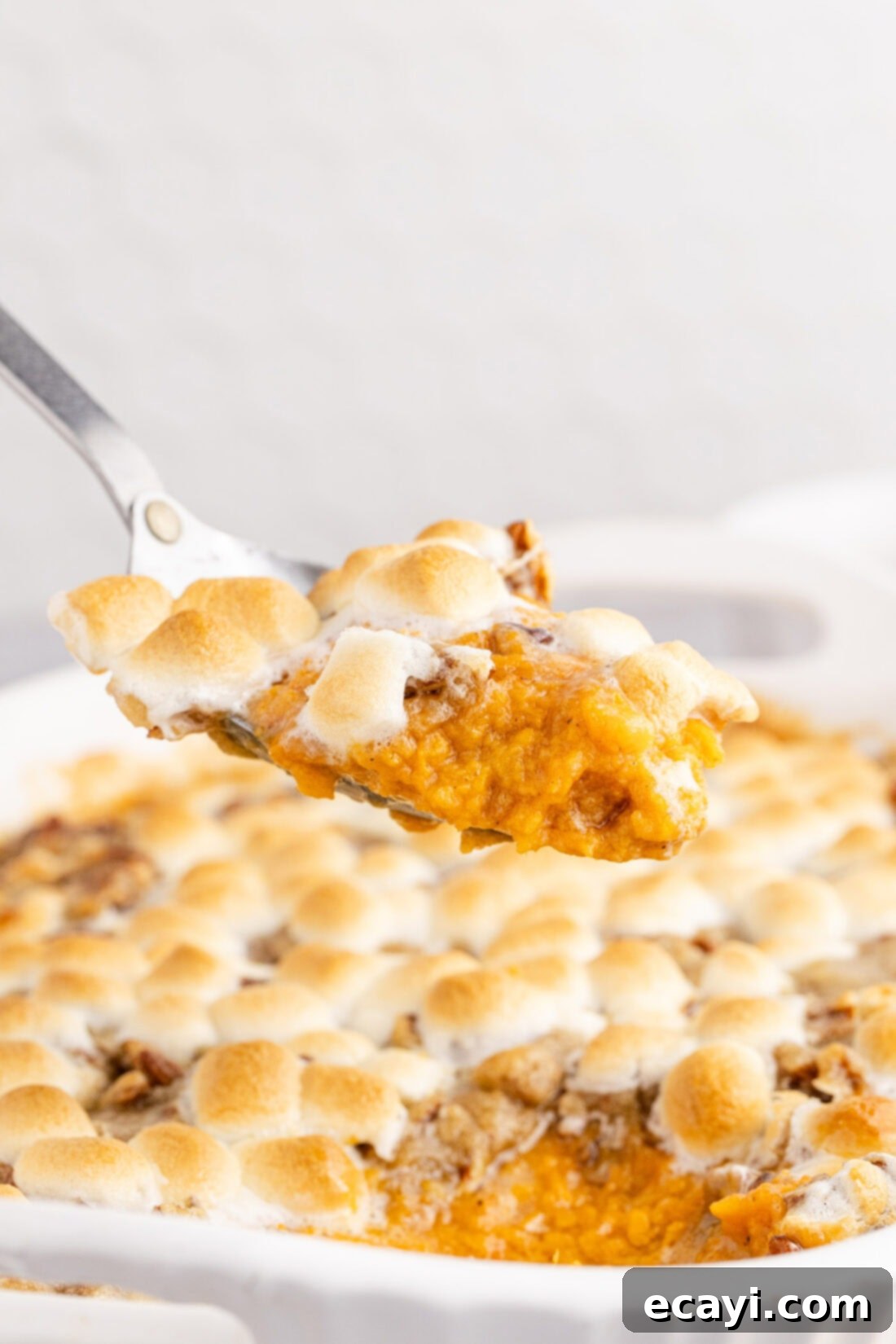 Golden Sweet Potato Bliss 3 Spoonful of Sweet Potato Casserole held above the baking dish, showing off the golden-brown marshmallow and pecan streusel topping.