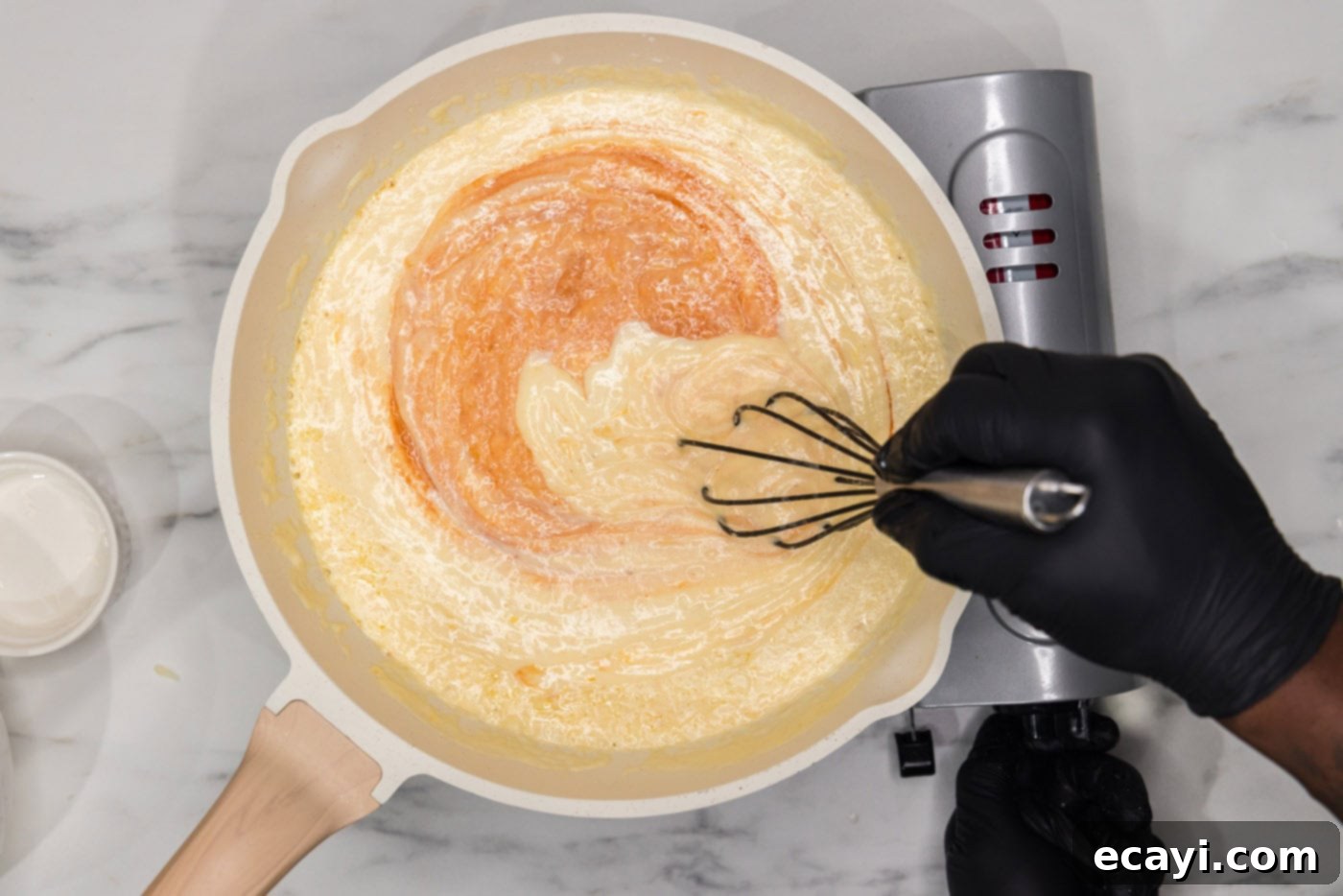 Buffalo Mac Bliss 9 whisking hot sauce into mac and cheese sauce in a skillet
