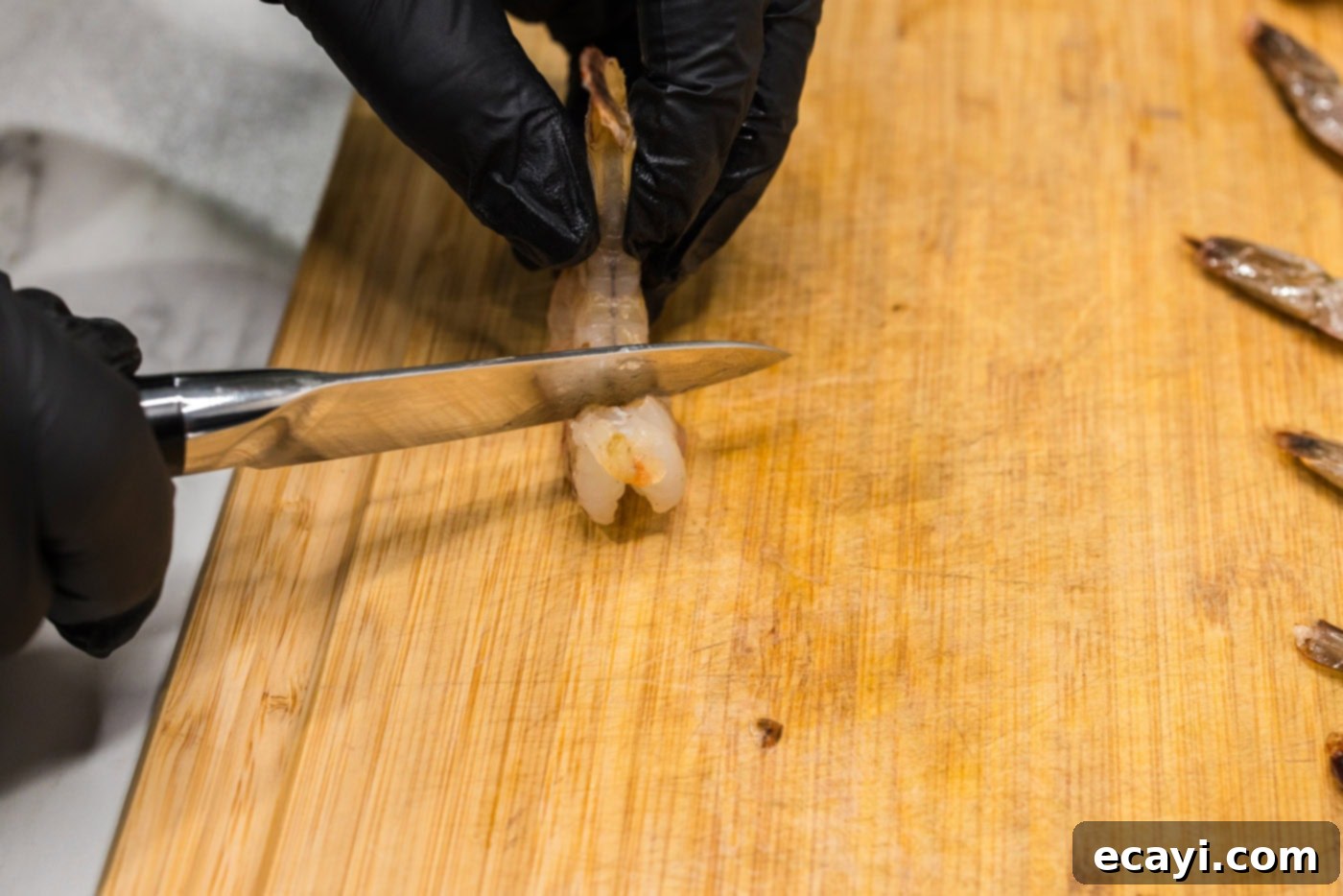 Crispy Air Fryer Bacon Wrapped Shrimp 5 scoring shrimp with a knife on a cutting board to prevent curling