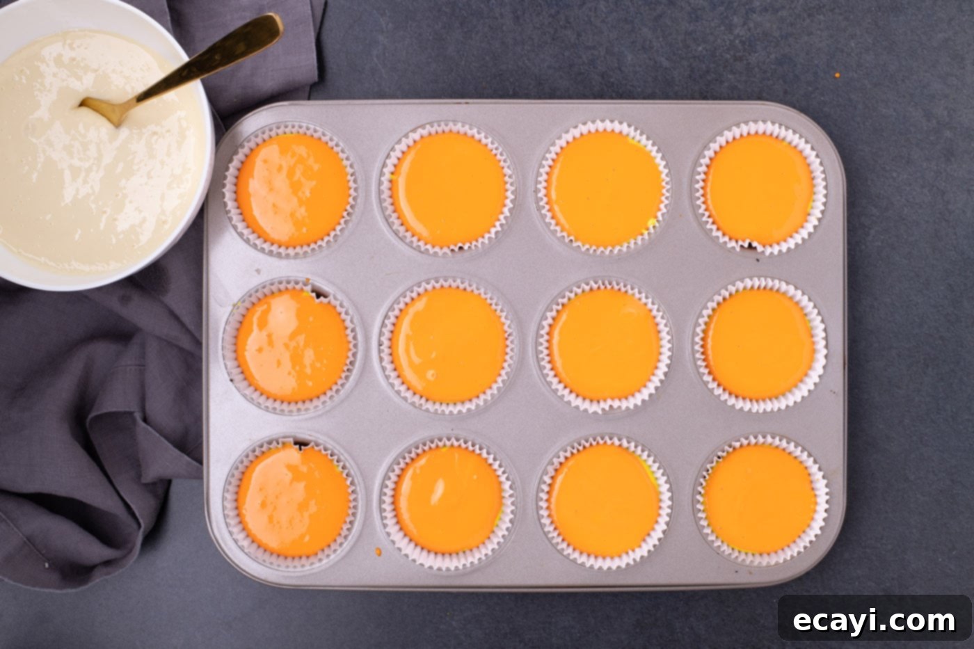 Festive Candy Corn Mini Cheesecakes 11 Orange cheesecake batter layered over yellow batter in cupcake liners within a muffin pan.