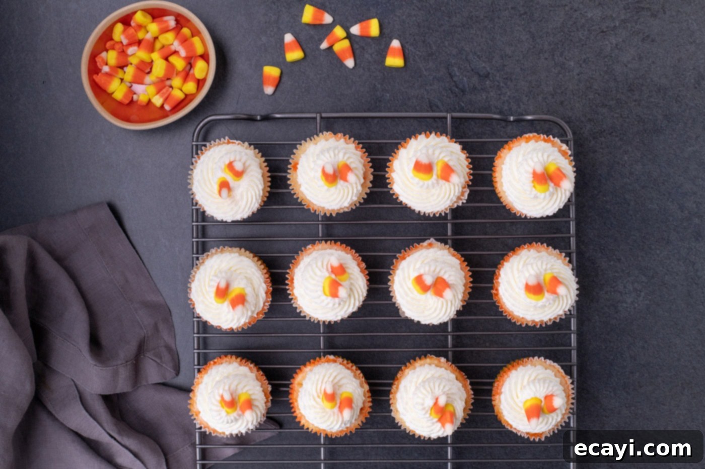 Festive Candy Corn Mini Cheesecakes 15 Finished candy corn cheesecakes arranged on a wire cooling rack, topped with swirls of whipped cream and garnished with candy corn.