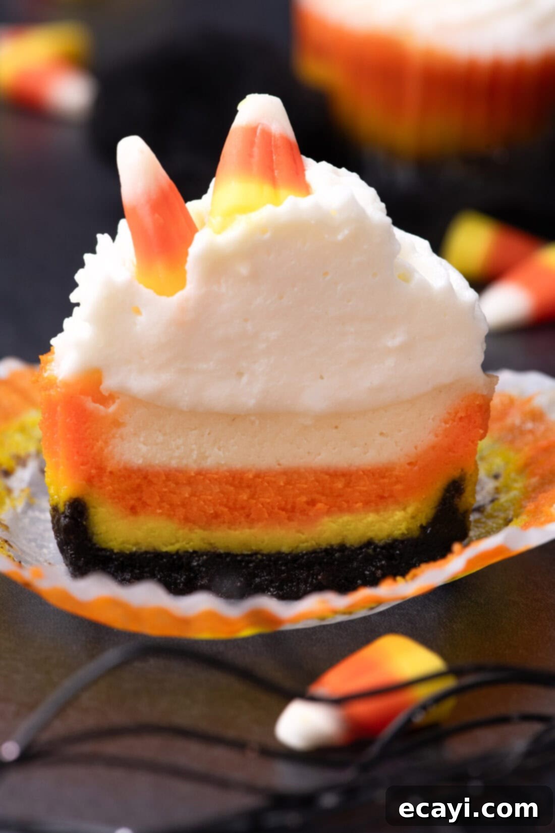 Festive Candy Corn Mini Cheesecakes 16 A mini candy corn cheesecake cut in half, revealing the distinct yellow, orange, and white layers of creamy cheesecake on top of the dark Oreo crust.