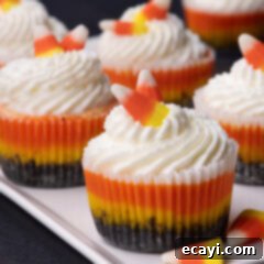 Festive Candy Corn Mini Cheesecakes 17 Close up photo of Mini Candy Corn Cheesecakes on a white platter, showing the distinct yellow, orange, and white layers with whipped cream and candy corn on top.