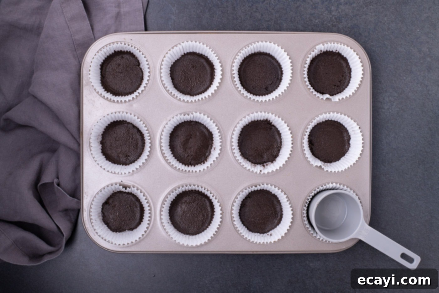 Festive Candy Corn Mini Cheesecakes 5 Oreo cookie crust mixture being pressed into cupcake liners in a muffin pan.