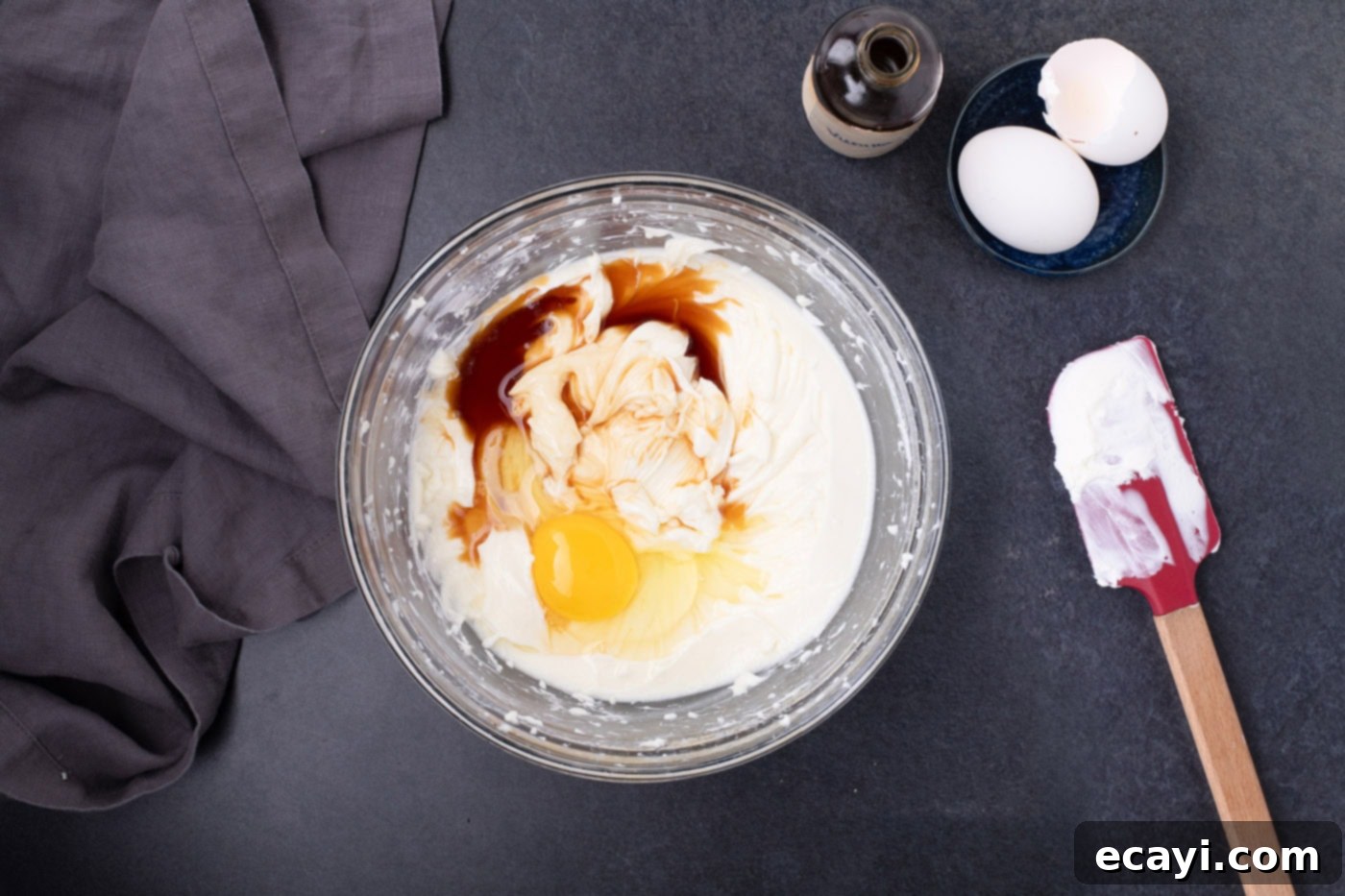 Festive Candy Corn Mini Cheesecakes 8 Eggs and vanilla extract are gently stirred into the creamy cheesecake batter in a large mixing bowl, ensuring minimal air incorporation.