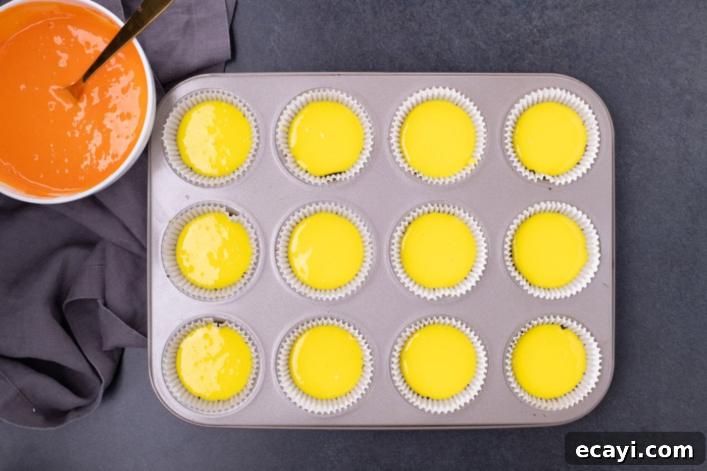 Festive Candy Corn Mini Cheesecakes 10 A muffin pan with cupcake liners, each containing a layer of vibrant yellow cheesecake batter on top of the Oreo crust.