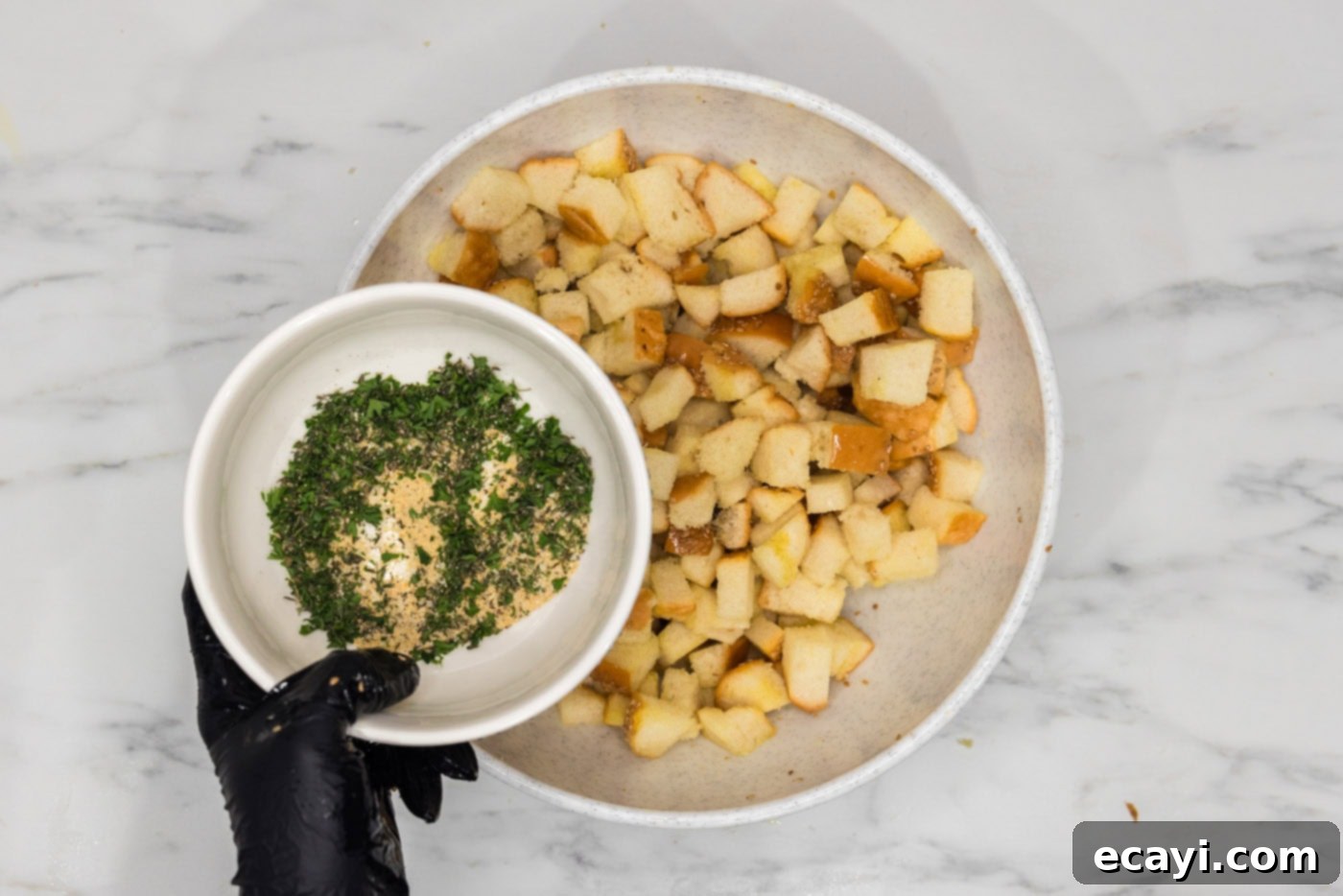 Crispy Golden Croutons 8 bowl of seasonings and herbs held over a bowl of cubed bread