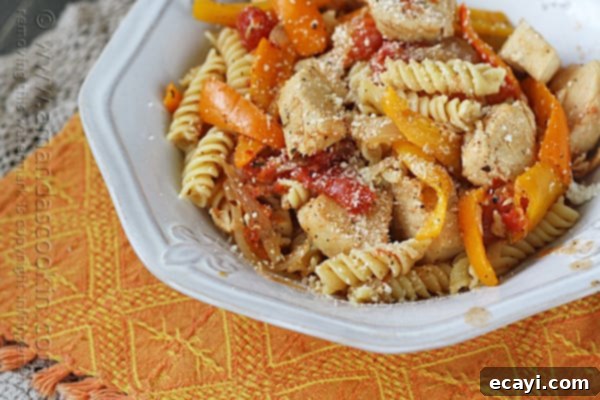 Savory Chicken and Pepper Pasta 18 A close up photo of chicken with peppers and pasta in a white bowl topped with Parmesan cheese.