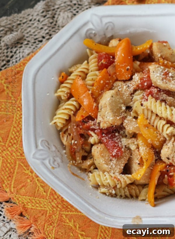 Savory Chicken and Pepper Pasta 3 A close up overhead photo of chicken with peppers and pasta in a white bowl topped with Parmesan cheese.