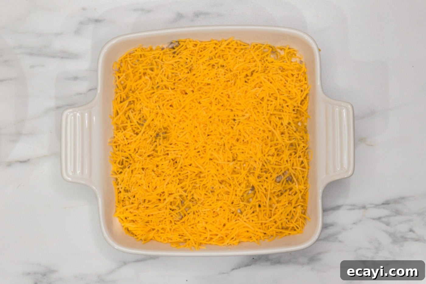 Loaded Cheeseburger Dip 13 shredded cheddar cheese on top of cheeseburger dip in a dish