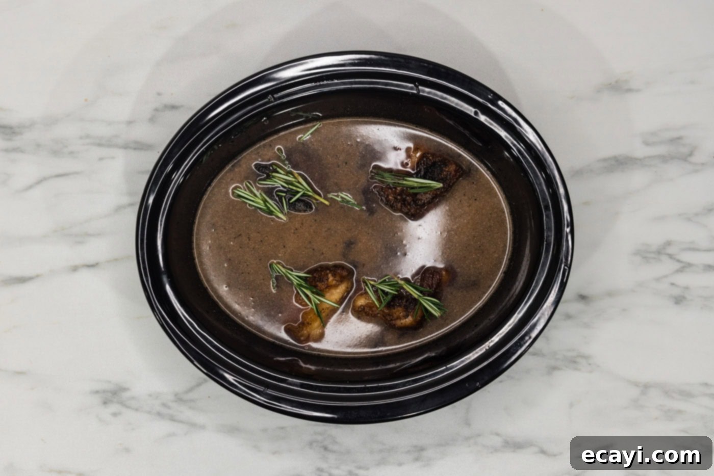 Rich & Tender Slow Cooker Short Ribs 9 rosemary sprigs on top of crockpot beef short ribs