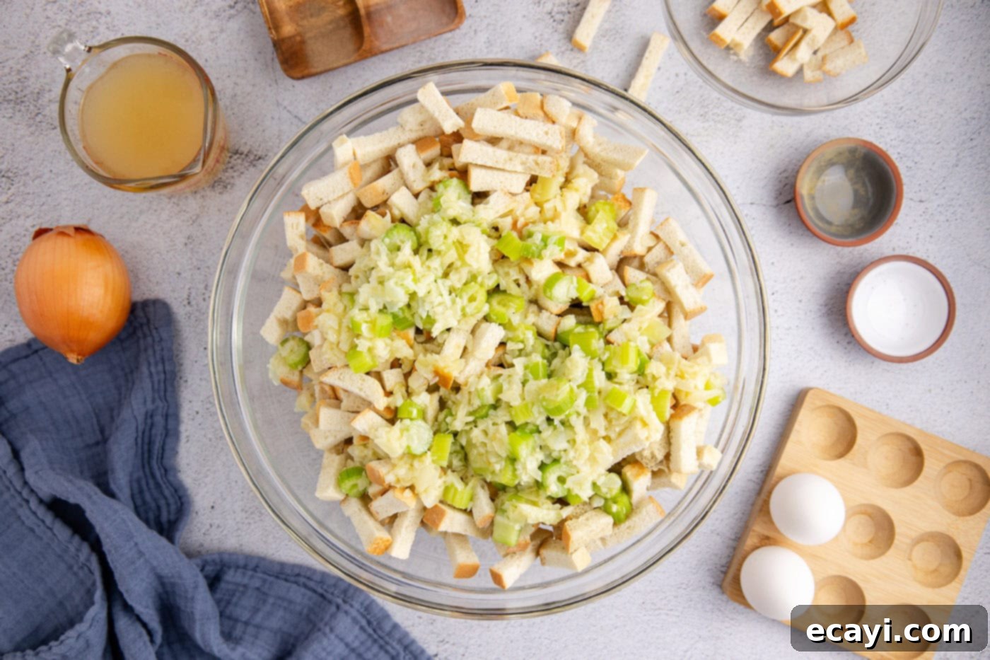 Easy Crockpot Stuffing 8 The sautéed celery and onion mixture being added to the dried bread cubes in a large mixing bowl.