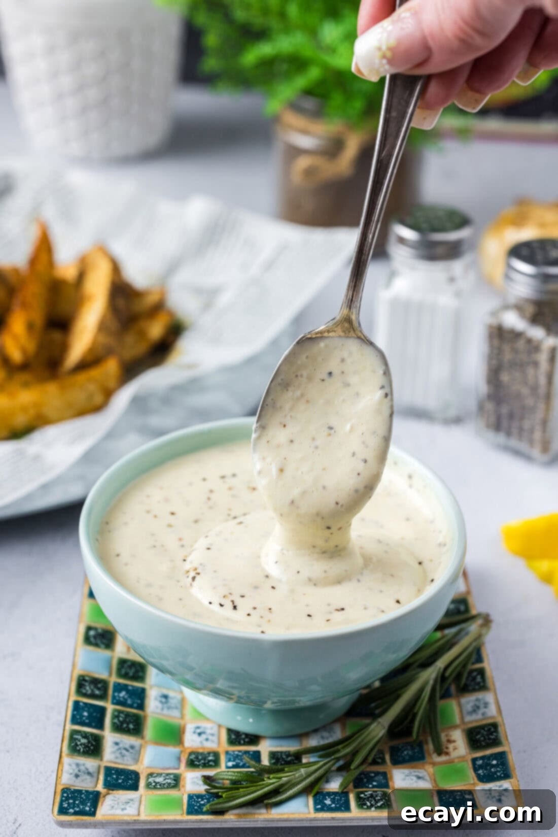 Creamy Garlic Aioli 2 Creamy Roasted Garlic Aioli gracefully falling off a spoon into a rustic bowl, showcasing its rich texture and inviting color.