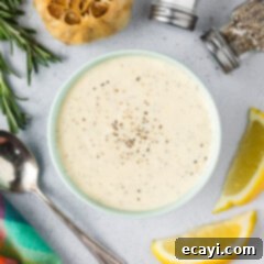 Creamy Garlic Aioli 8 Close up photo of a bowl of homemade Garlic Aioli with lemons, garlic, and seasonings around it on a rustic surface.