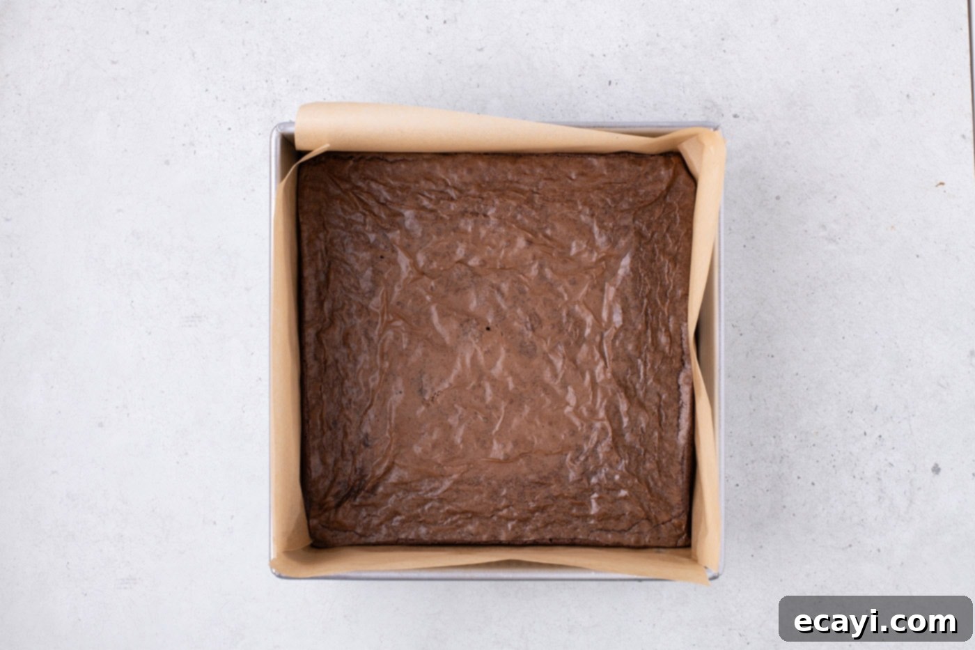 Decadent Pecan Pie Brownies 6 baked brownies cooling in a parchment lined baking pan, forming the base for the pecan pie topping