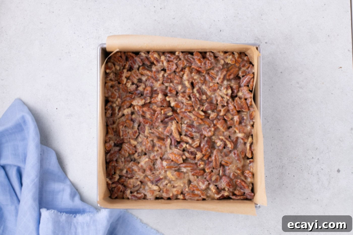 Decadent Pecan Pie Brownies 8 pecan pie topping spread evenly on top of baked brownies in a baking pan, ready for the final bake