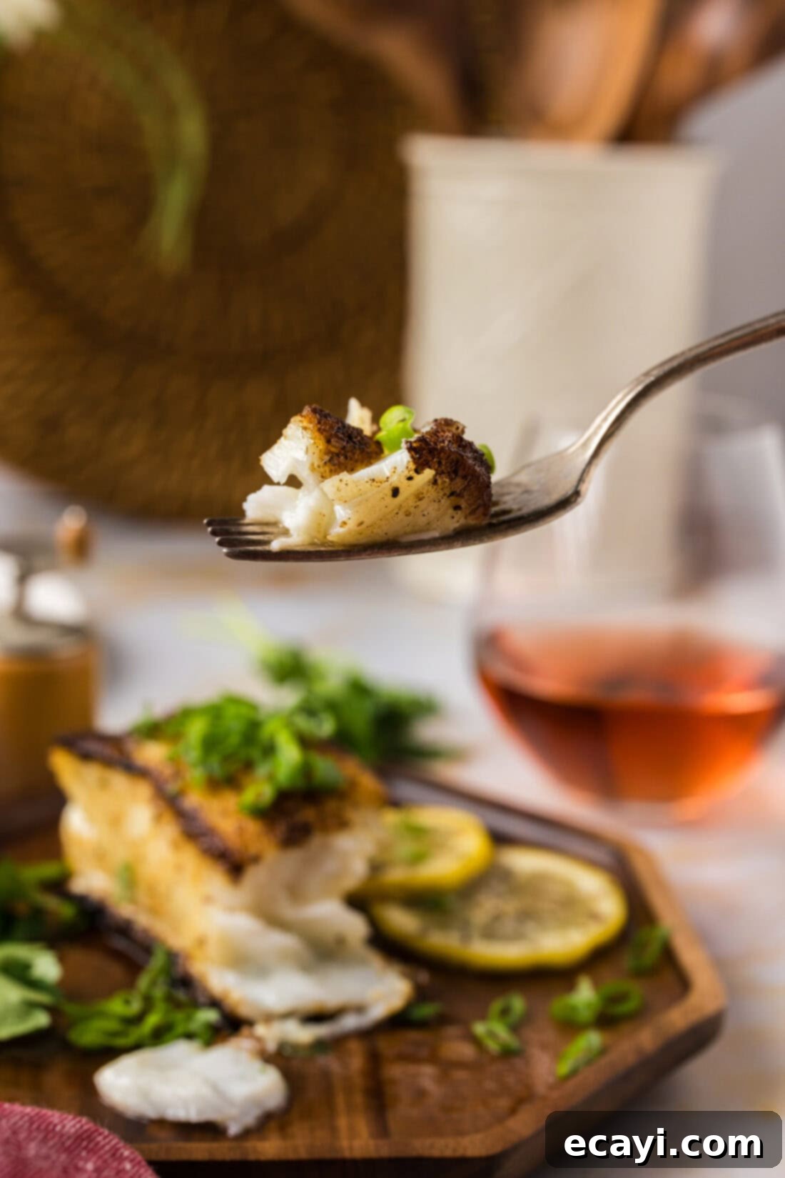 Crisp Skin Pan Seared Chilean Sea Bass 11 Piece of Pan Seared Chilean Sea Bass on a fork held above a plate of Pan Seared Chilean Sea Bass