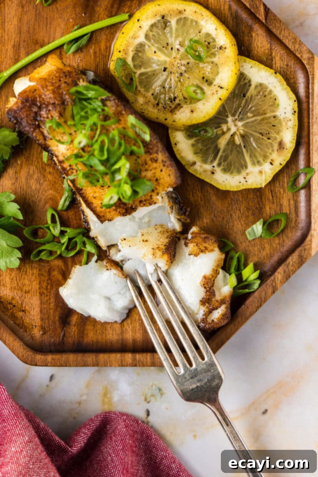 Crisp Skin Pan Seared Chilean Sea Bass 3 Overhead photo of a Pan Seared Chilean Sea Bass filet on a plate with a fork and lemons on the side