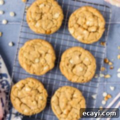 Decadent White Chocolate Macadamia Delights 12 Close-up photo of freshly baked White Chocolate Macadamia Nut Cookies, still warm and cooling on a wire rack, highlighting their perfectly golden edges and visible chunks of white chocolate and nuts.