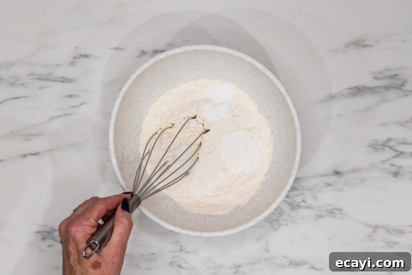 Decadent White Chocolate Macadamia Delights 5 A hand whisking together dry ingredients including flour, baking powder, baking soda, and salt in a mixing bowl, ensuring they are well combined before adding to wet ingredients.