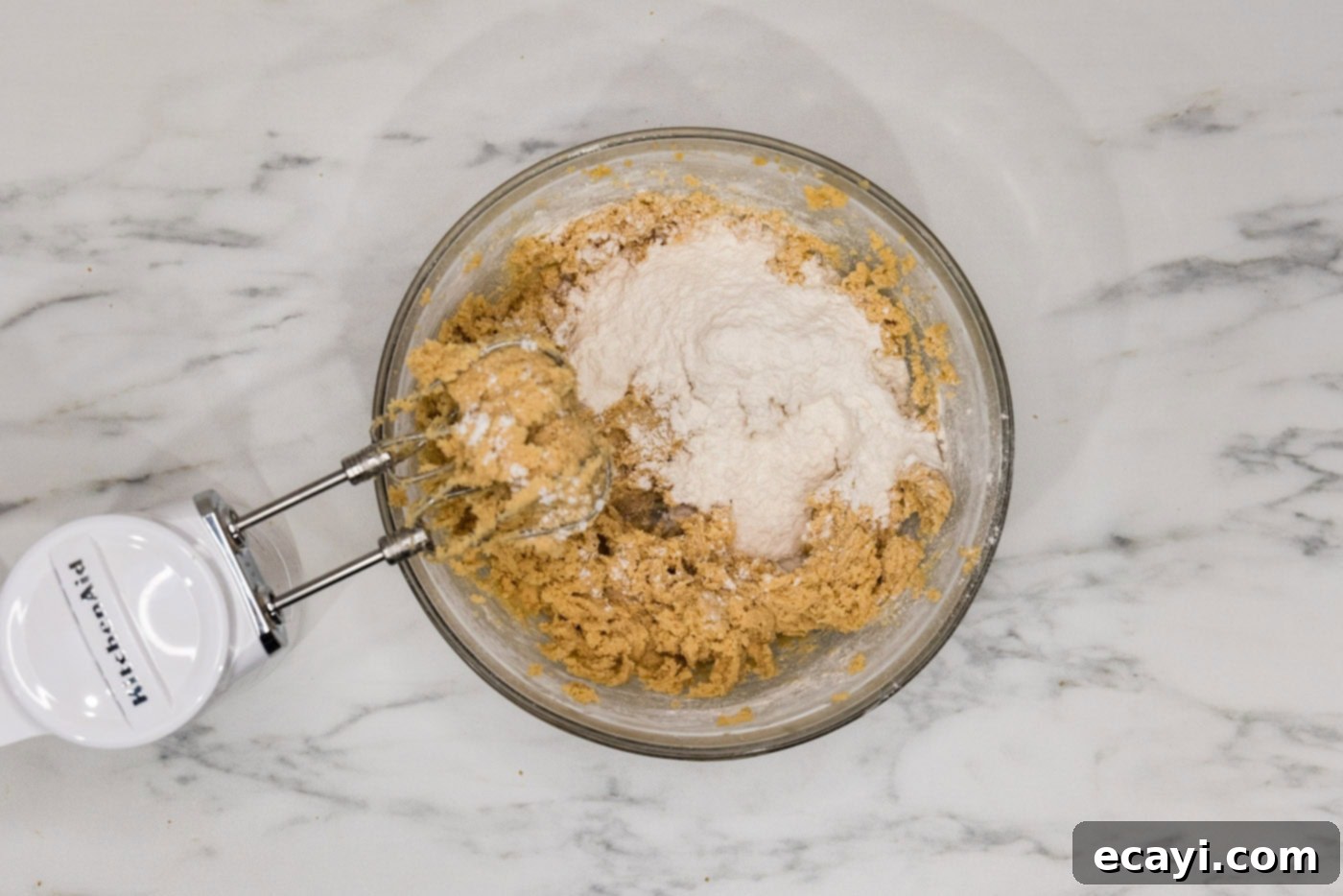 Decadent White Chocolate Macadamia Delights 7 A hand mixer blending dry ingredients into wet cookie dough on a low setting, ensuring minimal gluten development for tender cookies.