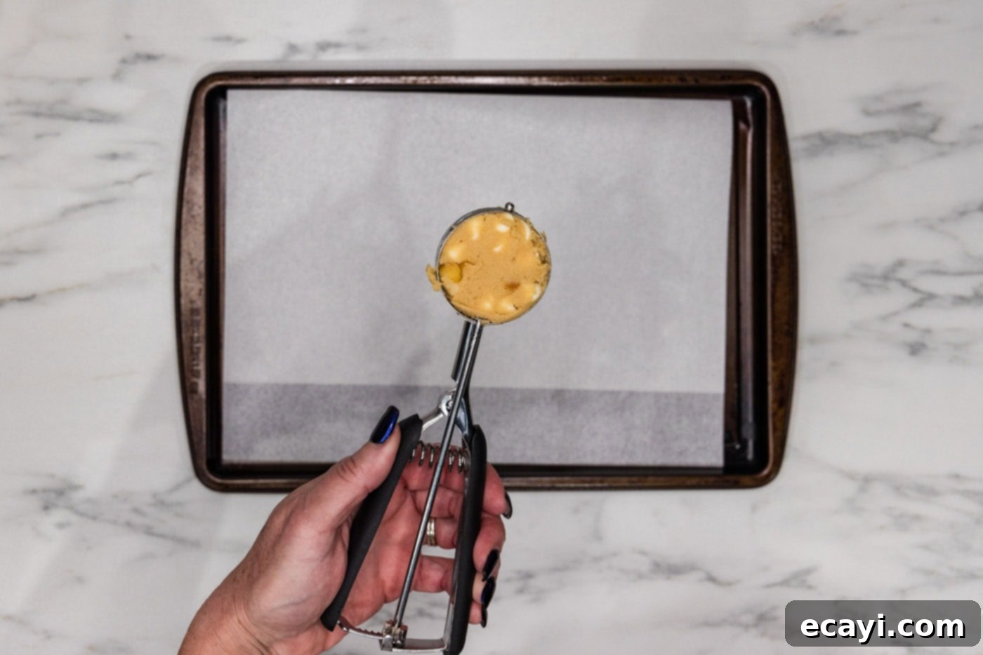 Decadent White Chocolate Macadamia Delights 9 A 3-tablespoon cookie scoop filled with white chocolate macadamia nut cookie dough, ready to be placed on a baking sheet for baking.
