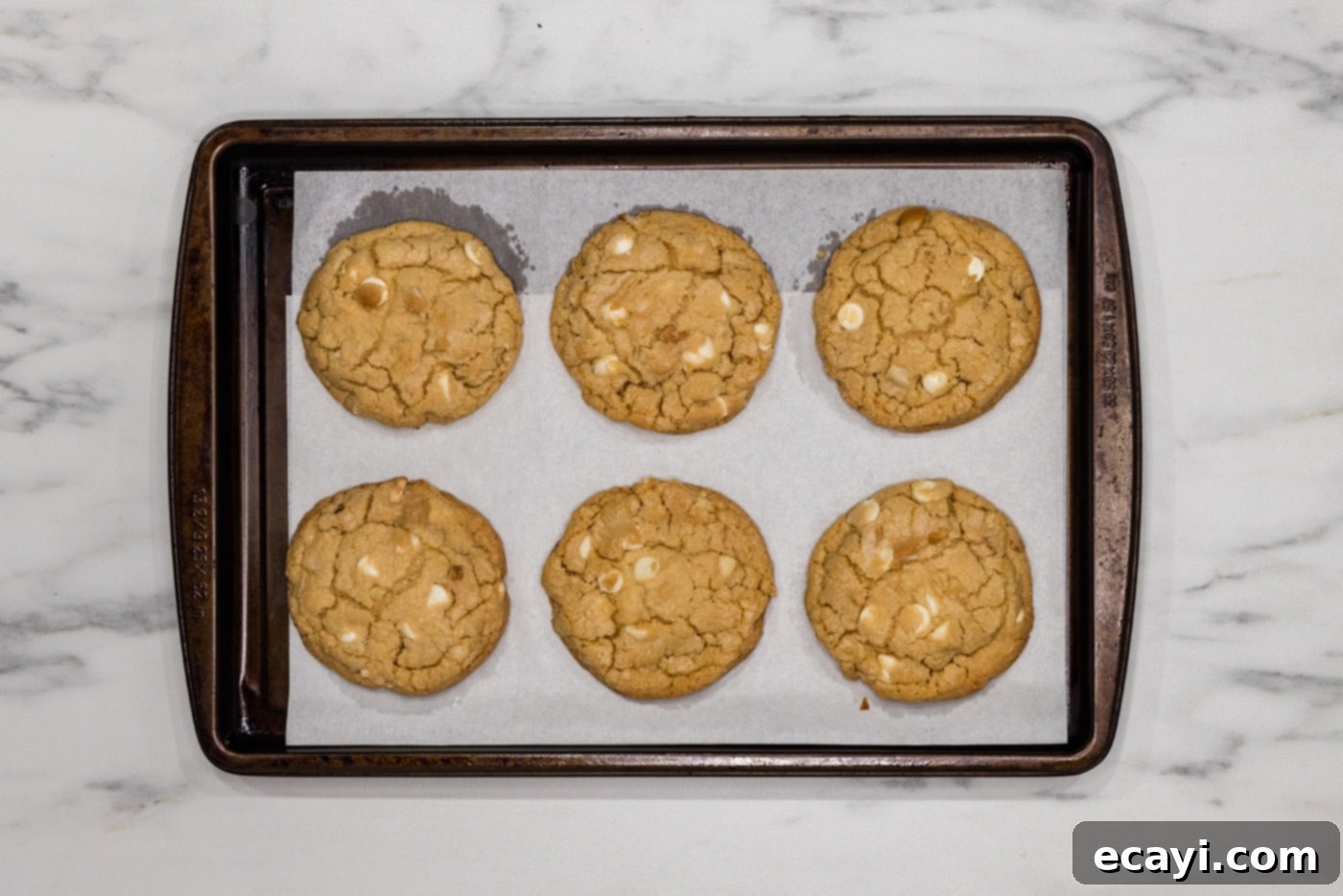 Decadent White Chocolate Macadamia Delights 10 A batch of freshly baked white chocolate macadamia nut cookies cooling on a baking sheet, with their edges lightly browned and centers soft.