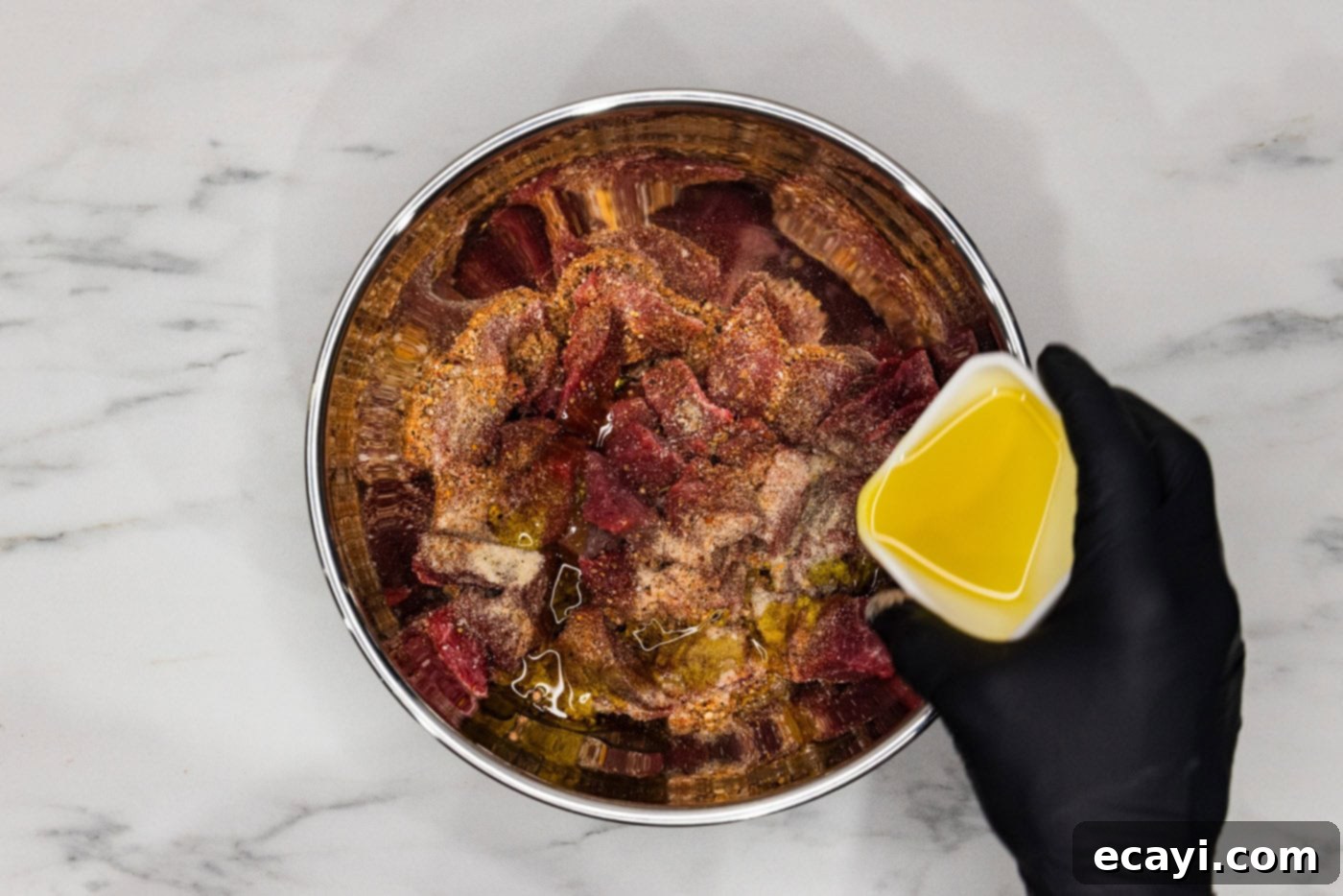 Mouthwatering Garlic Butter Steak Bites 6 Pouring olive oil into a bowl containing cubed steak and various seasonings, illustrating the mixing process.