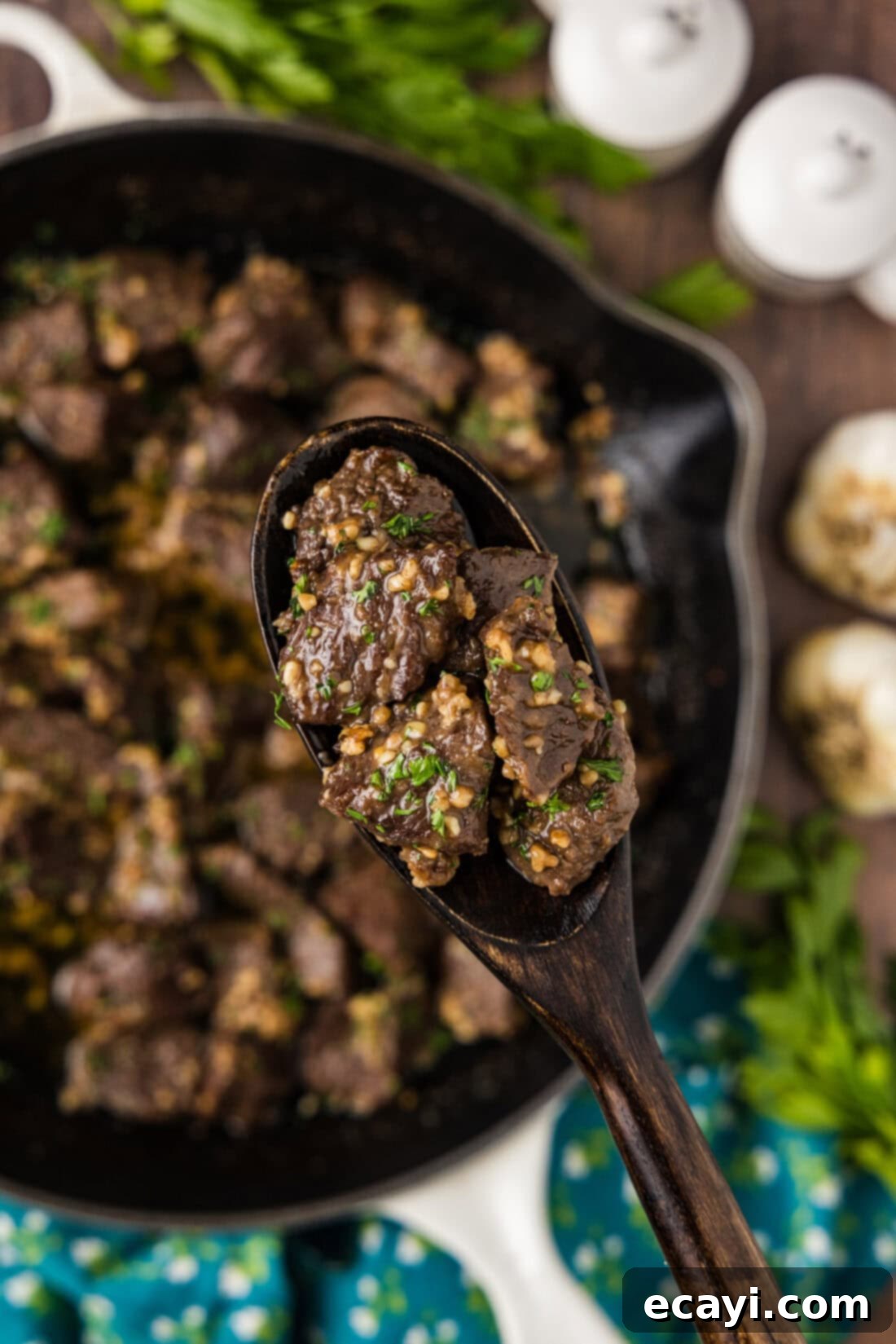 Mouthwatering Garlic Butter Steak Bites 10 A spoonful of Garlic Butter Steak Bites is held above a skillet, showing the tender steak pieces coated in sauce.