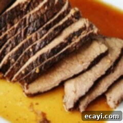 Velvet Brandy Pot Roast 11 A close up of sliced slow cooker roast with brandy sauce on a white platter.
